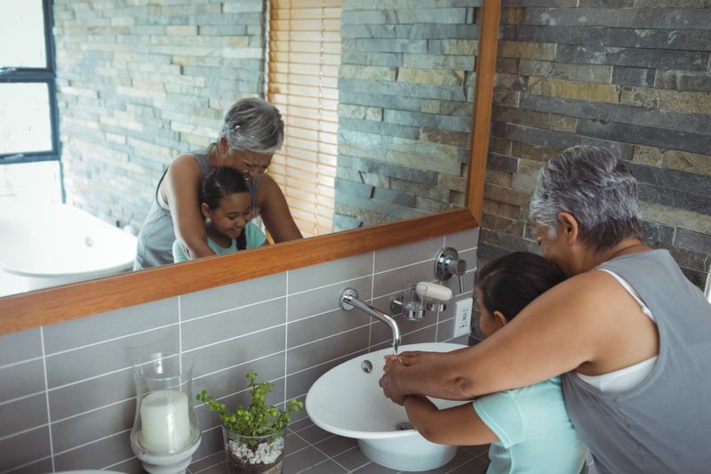 Grandmother and granddaughter washing hands in bathroom sink