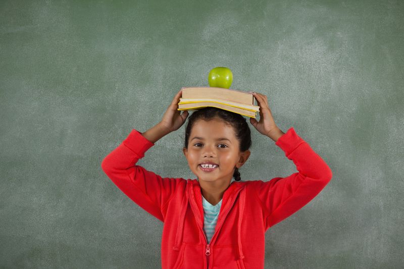 Young girl balancing books and apple on her head