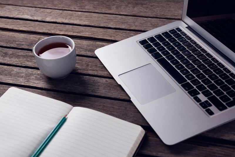 Laptop, black coffee and diary on wooden table