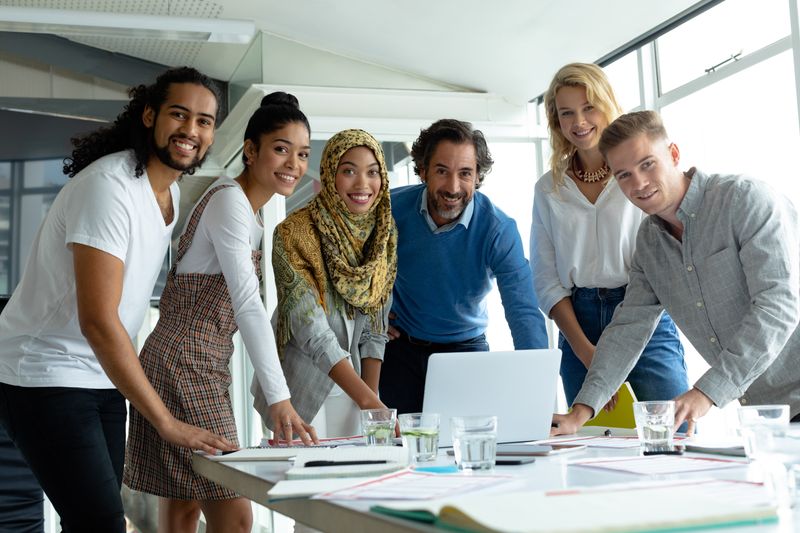 Front view of diverse business people looking at camera while working together at conference room in a modern office