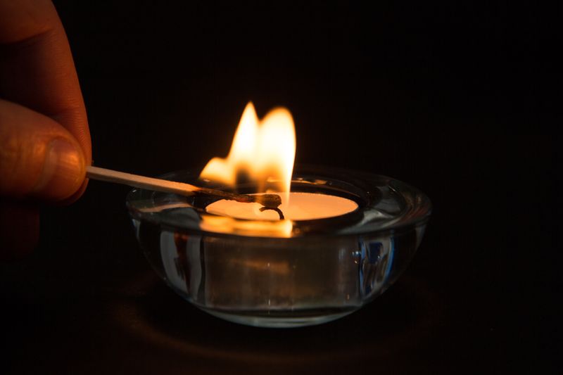 Hand lighting tea light candle in the dark