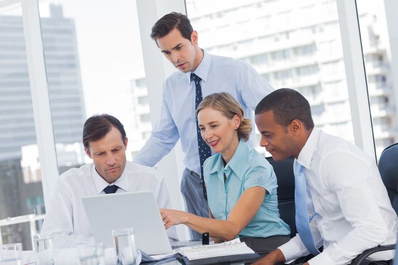 Four business people in a meeting room watching a laptop