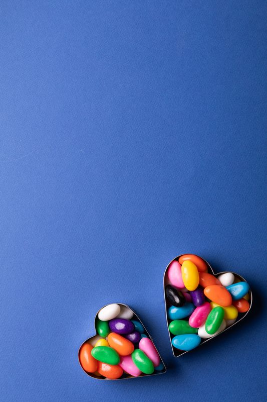 Overhead view of copy space above colorful candies in heart shape containers over blue background