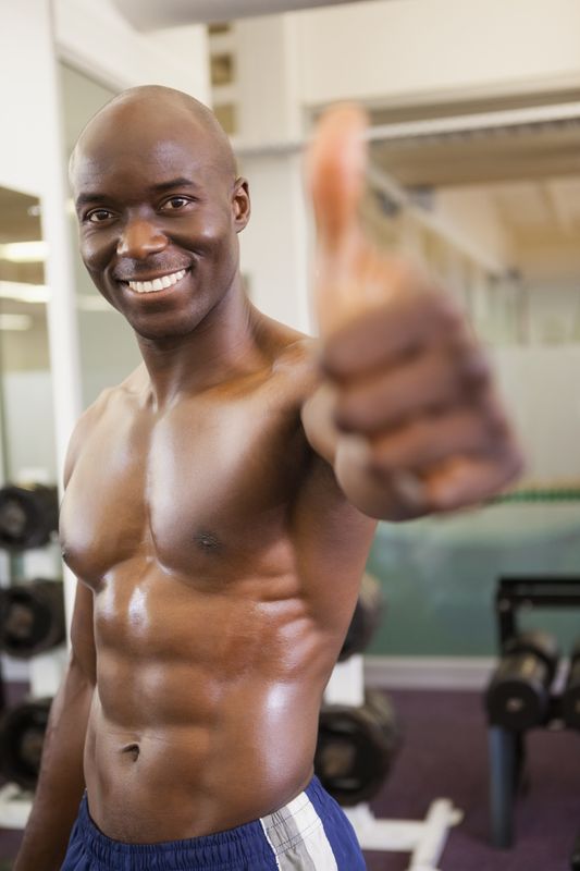 Shirtless muscular man giving thumbs up in gym