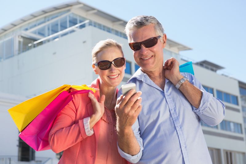 Happy senior couple looking at smartphone holding shopping bags