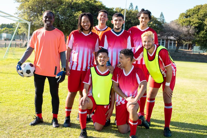 Portrait of happy male soccer team players wearing uniforms posing in playground during sunny day. Summer, ball, unaltered, soccer, sport, team sport, togetherness and competition concept.