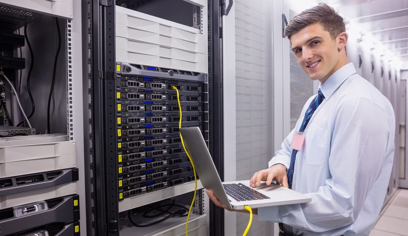 Smiling technician using laptop while analysing server