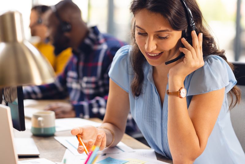 Diverse business people sitting at desks and using phone headsets at office. Casual business, communication and work, unaltered.