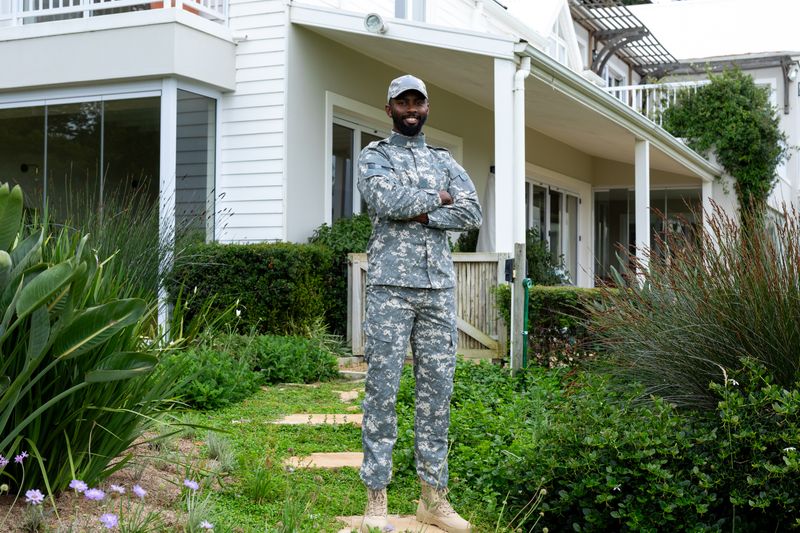 Portrait of happy african american male soldier wearing military uniform staying against house