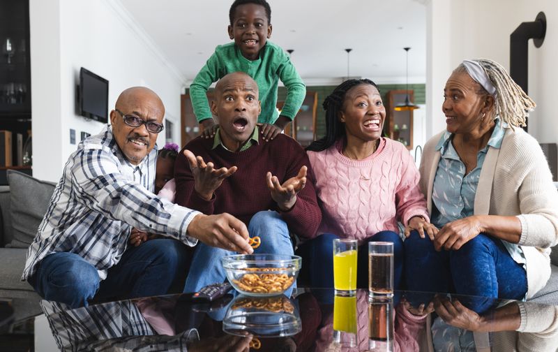 Excited african american parents, son and grandparents watching sport on tv, slow motion. Sport, entertainment, home, family, togetherness, domestic life and lifestyle, unaltered.