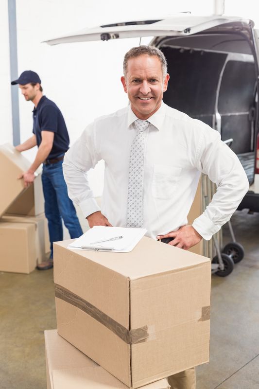 Smiling manager standing behind stack of cardboard boxes