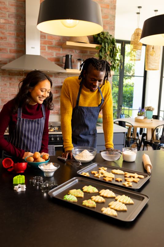 Happy diverse couple admiring freshly baked christmas cookies in kitchen, copy space