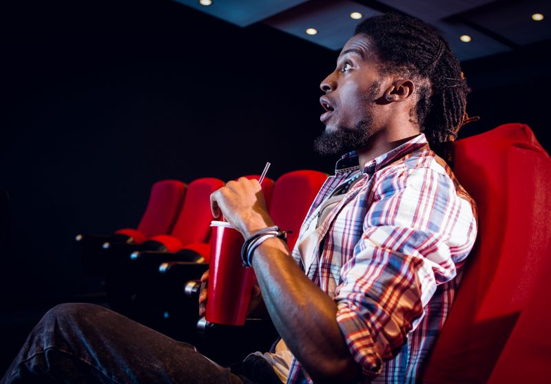 Young man watching a film and drinking soda