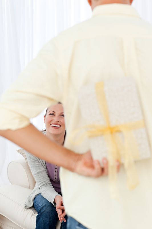 Happy man hiding a present for his girlfriend waiting on the sofa