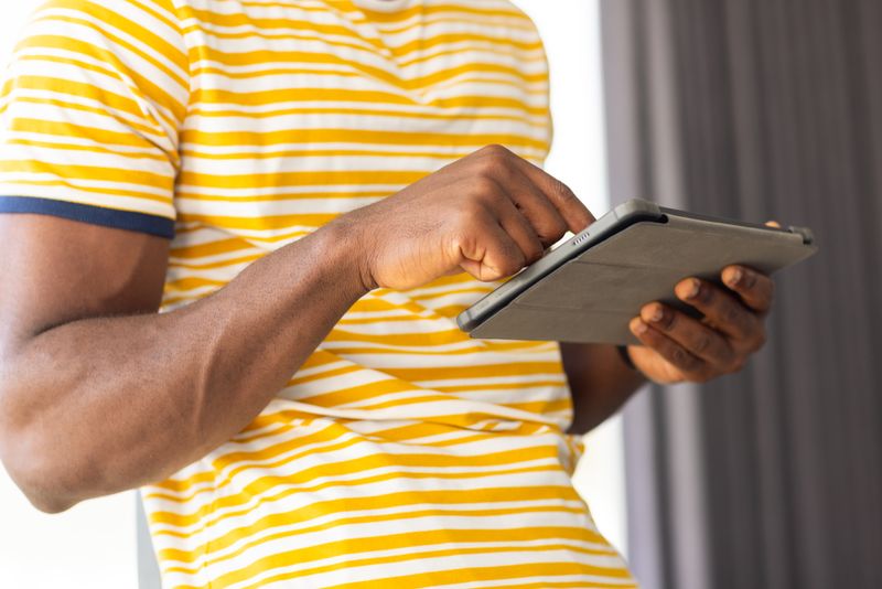 Using tablet, man in striped shirt browsing or working at home. Technology, remote work, lifestyle, digital device, home office, casual, unaltered