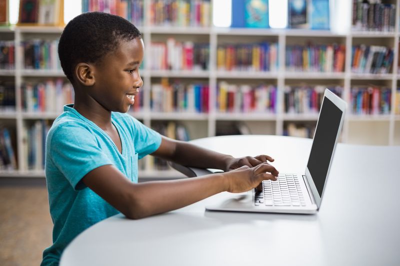 Schoolboy using laptop in library