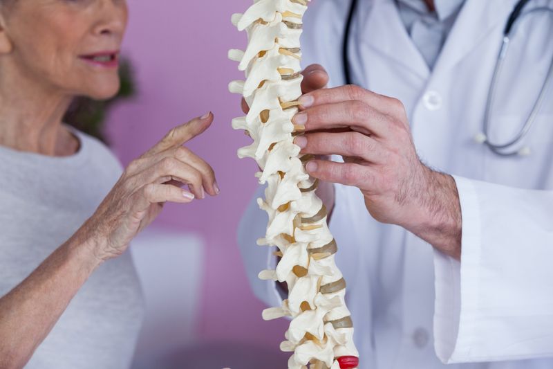 Mid section of physiotherapist explaining the spine model to patient