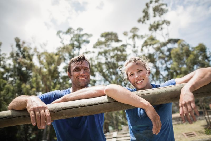 Smiling man and woman leaning on a hurdle during obstacle course