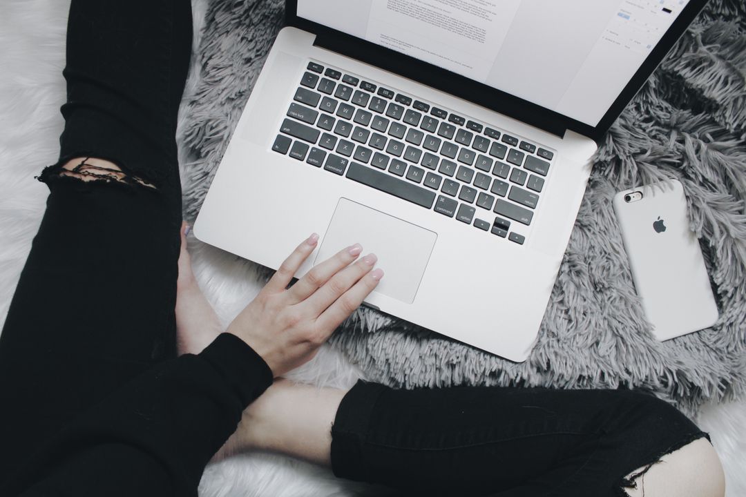 Woman using her laptop on a fur blanket with her phone - How to create engaging content for blogs - Image