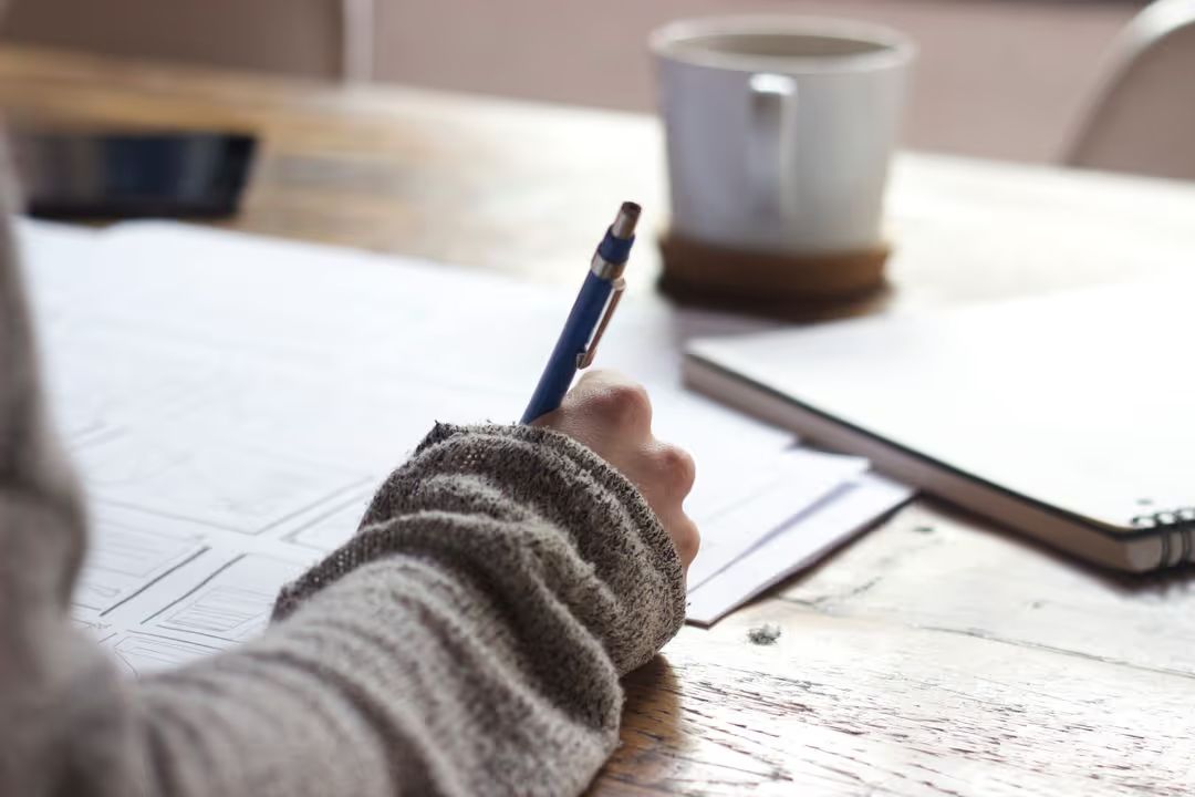 An image of a person holding a pen and writing something down - How to stay consistent in posting content on social media - Image