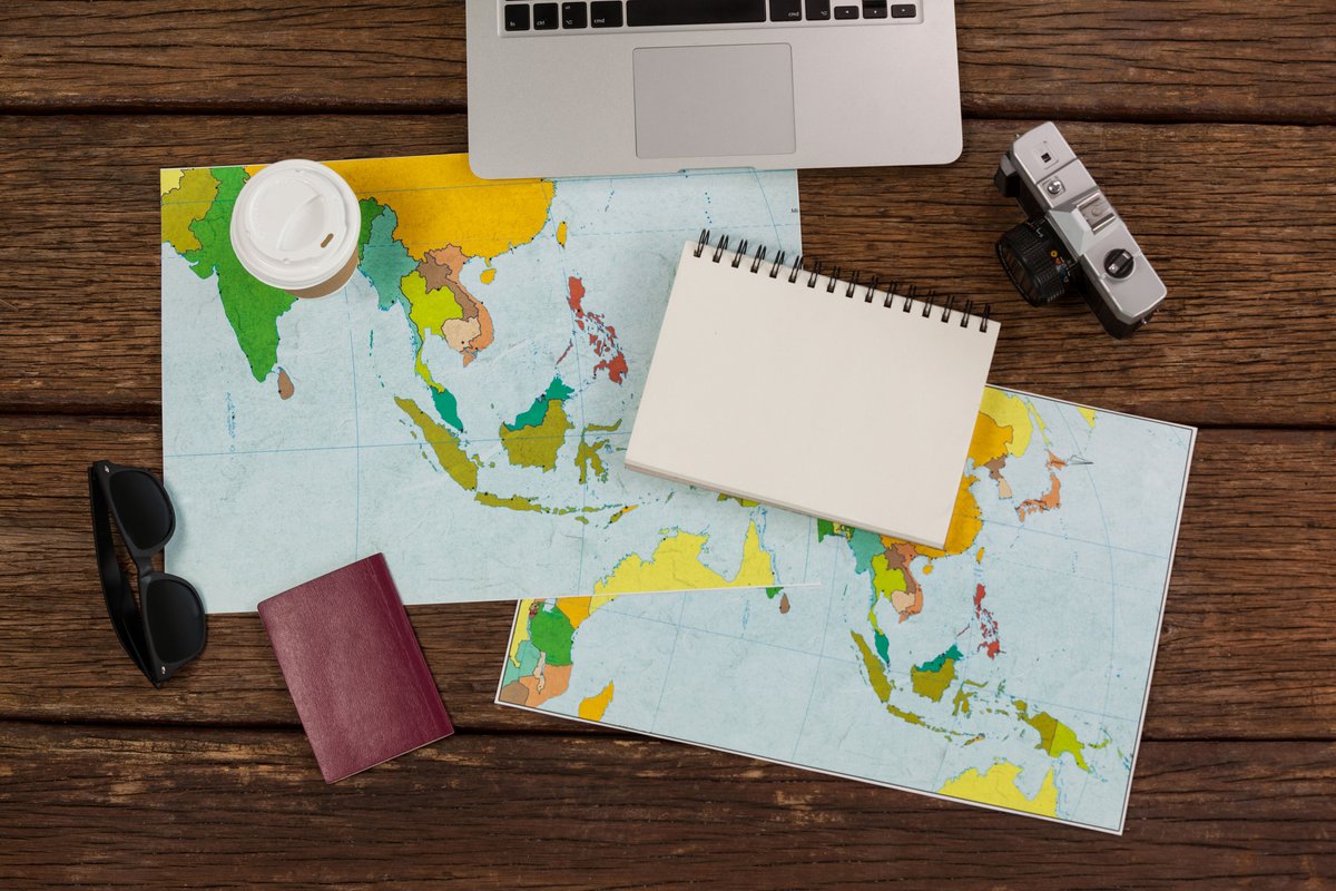 Image of a laptop, a map, a notebook, a passport, coffee and sunglasses on a desk - Guide to writing a travel blog - Image