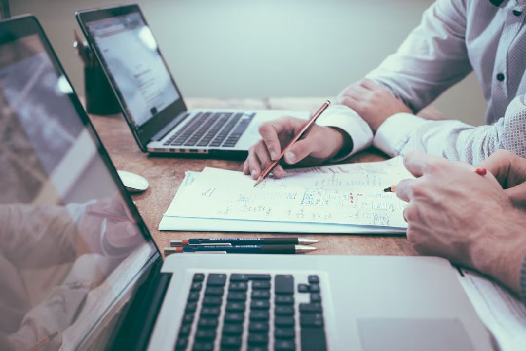 Side image of co-workers brainstorming on paper with a laptop in front of each of them - Simple but powerful tactics for crafting compelling ad copies that drive sales - Image