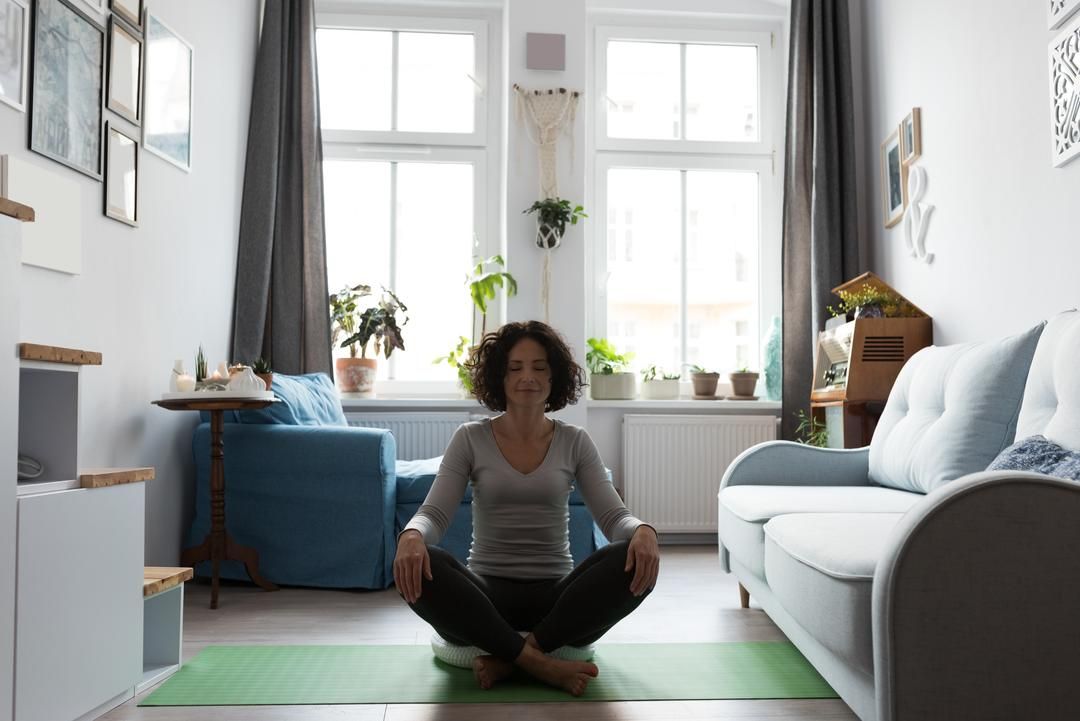 Woman doing yoga on a green mat in her living room, windows in the background - 35 creative YouTube video ideas when you're out of inspiration - Image