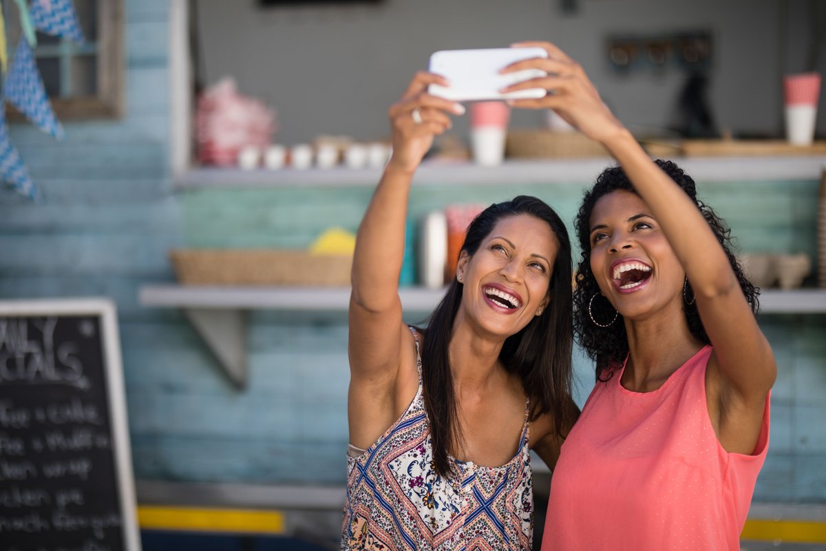 Two friends smiling taking a picture on smartphone - Tips on how to take attractive Instagram photos - Image
