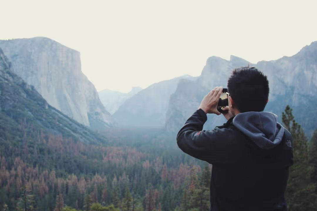 Image of a man taking a photograph of the landscape with his mobile phone - A selection of on trend background ideas for your next design in 2021 - Image