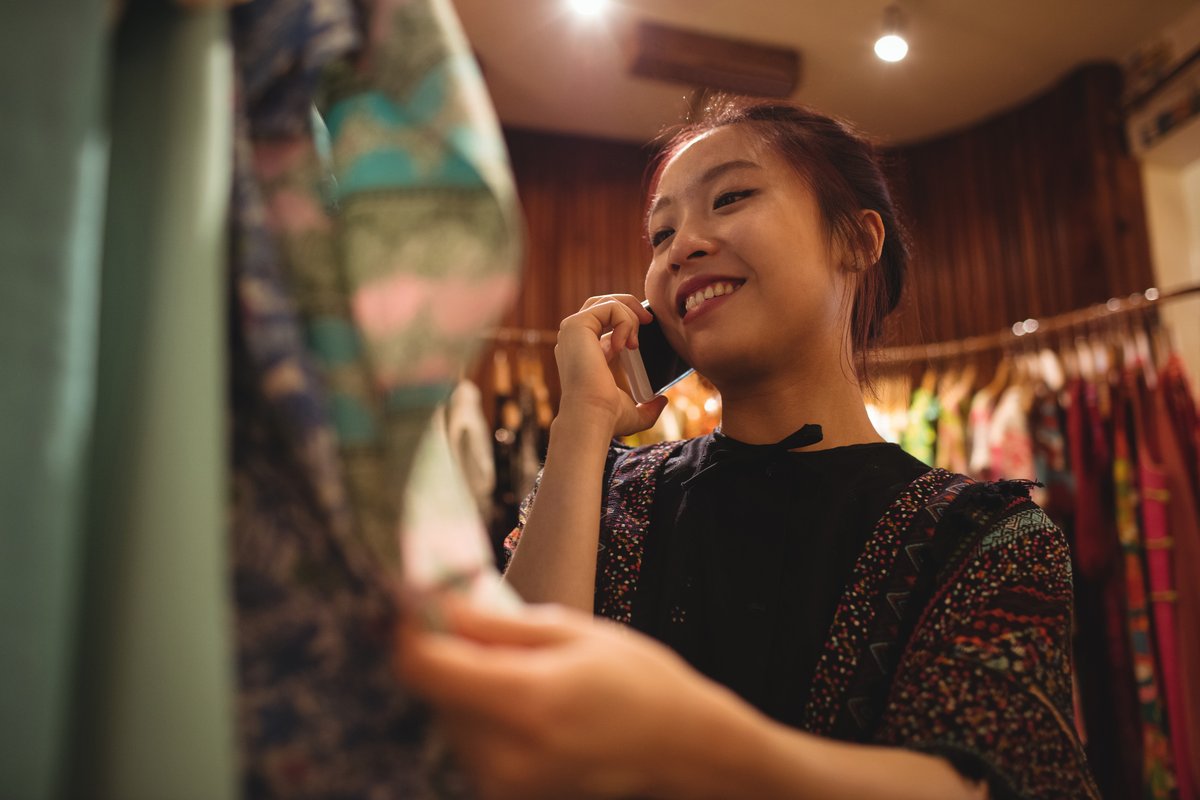 Woman on the phone smiling while looking at clothes - Retail marketing strategy tips and tricks to drive sales and save money - Image