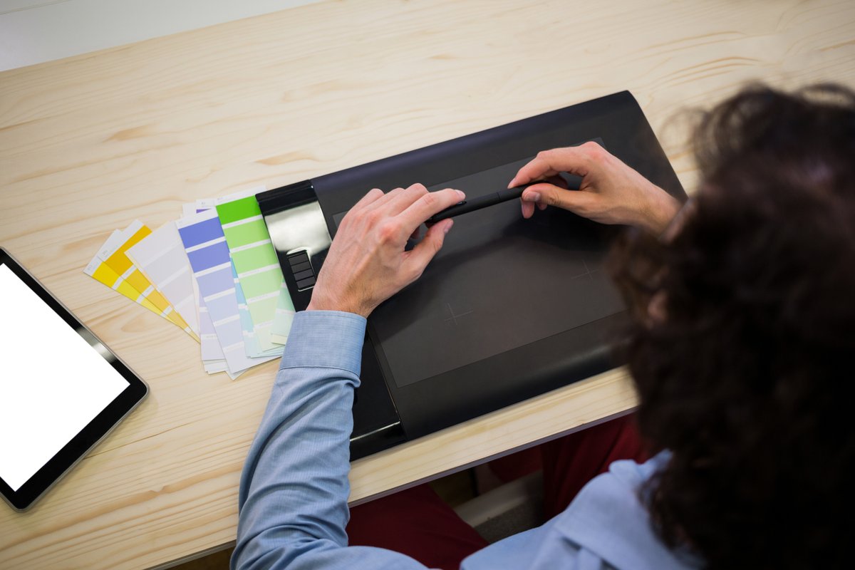A man holds a stylus pen over a drawing tablet - What you need to know to create the best graphics for your business - Image