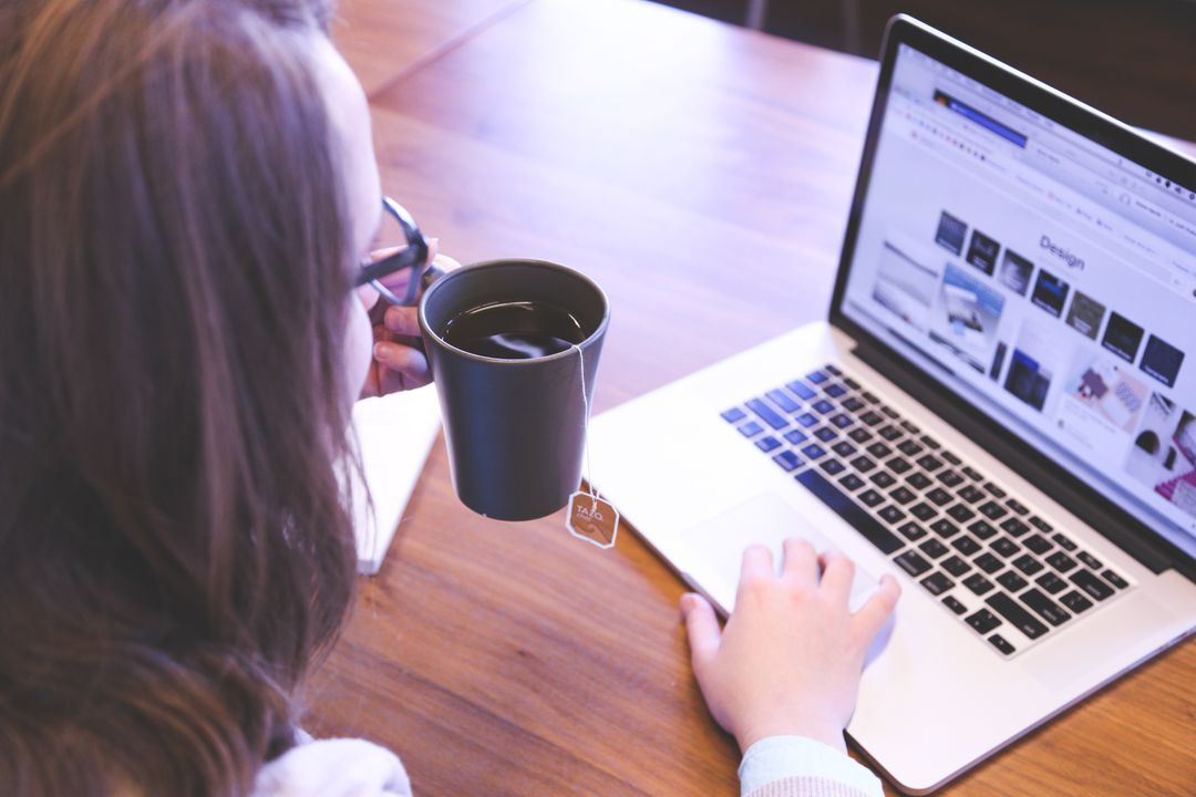 Woman drinking a cup of tea while working on a laptop - How to create engaging content for blogs - Image