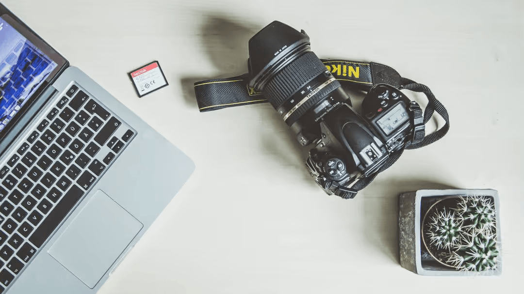 Overhead image of a laptop, camera, sd card and a cactus on a wooden desk - How to choose the perfect YouTube thumbnail size - Image