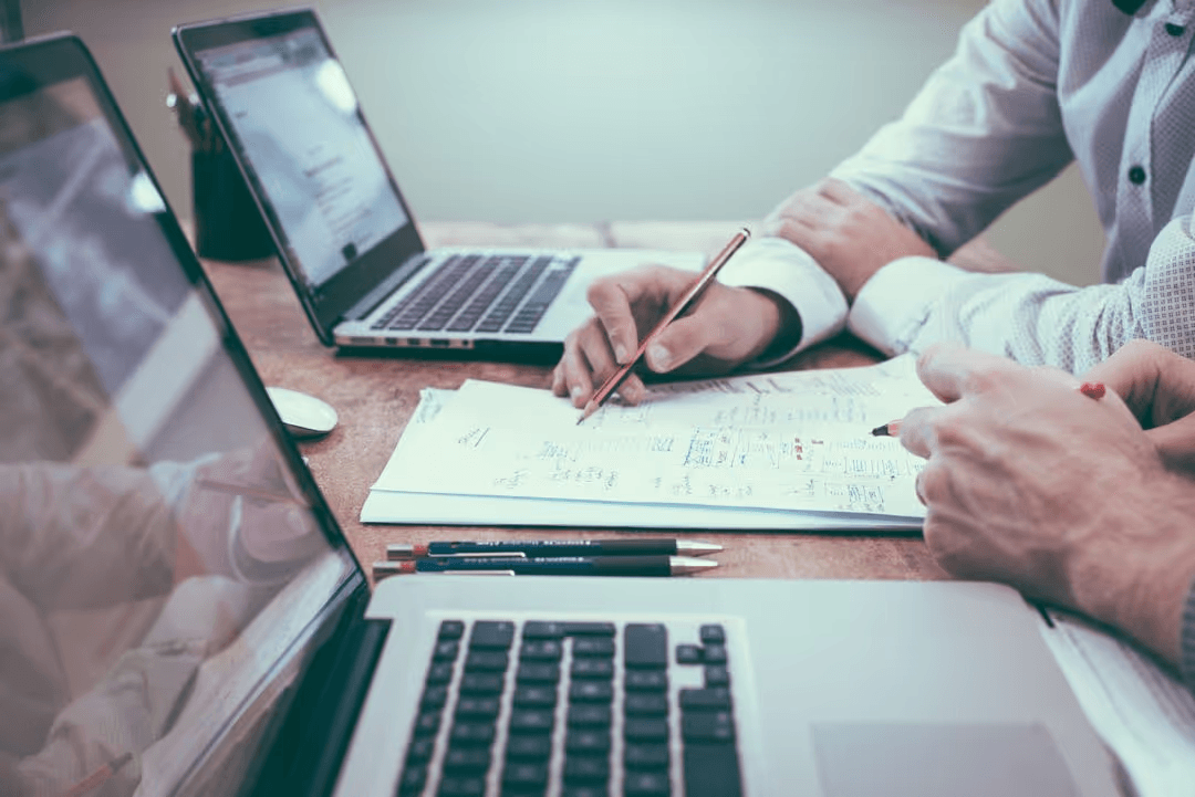 Image of a desk with two macbooks, notes and pens - Learn from your competitors - Image