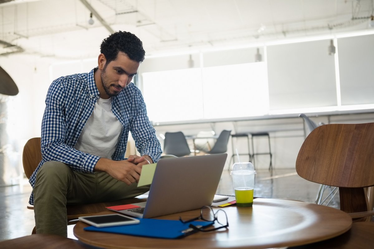 Man looking at his laptop on a table in an office - Five tips on how to become a successful business blogger - Image