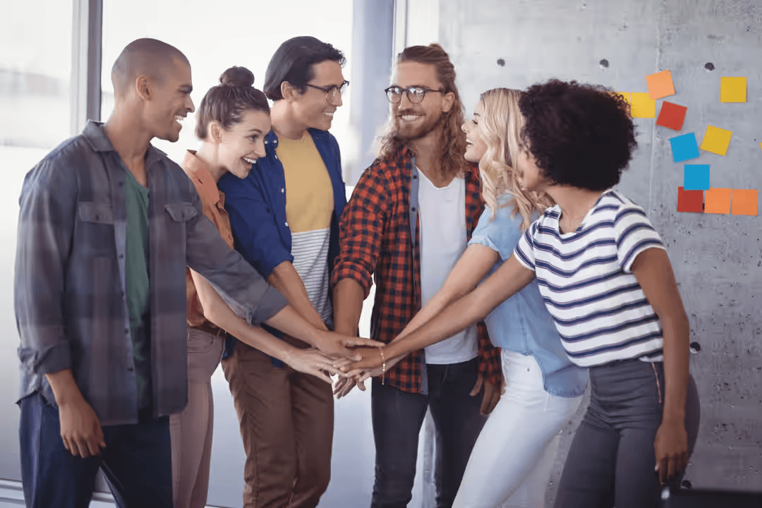 Group of employees with their hands stacked with whiteboard in the background with sticky notes - Retail marketing strategy tips and tricks to drive sales and save money - Image