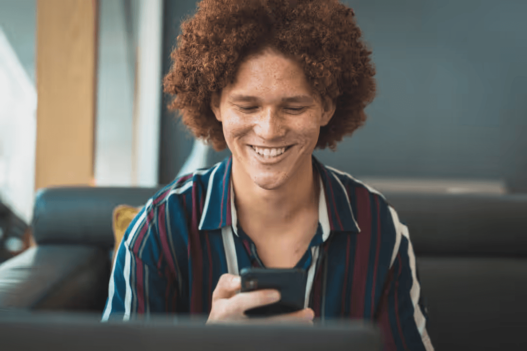 Person engaged with phone, laughing, sitting on a sofa - Expert online marketing tips to improve your digital strategy and make more money - Image