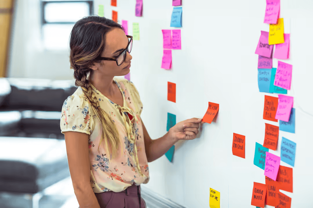 Image of a woman putting sticky notes on a whiteboard - How to create content themes - Image