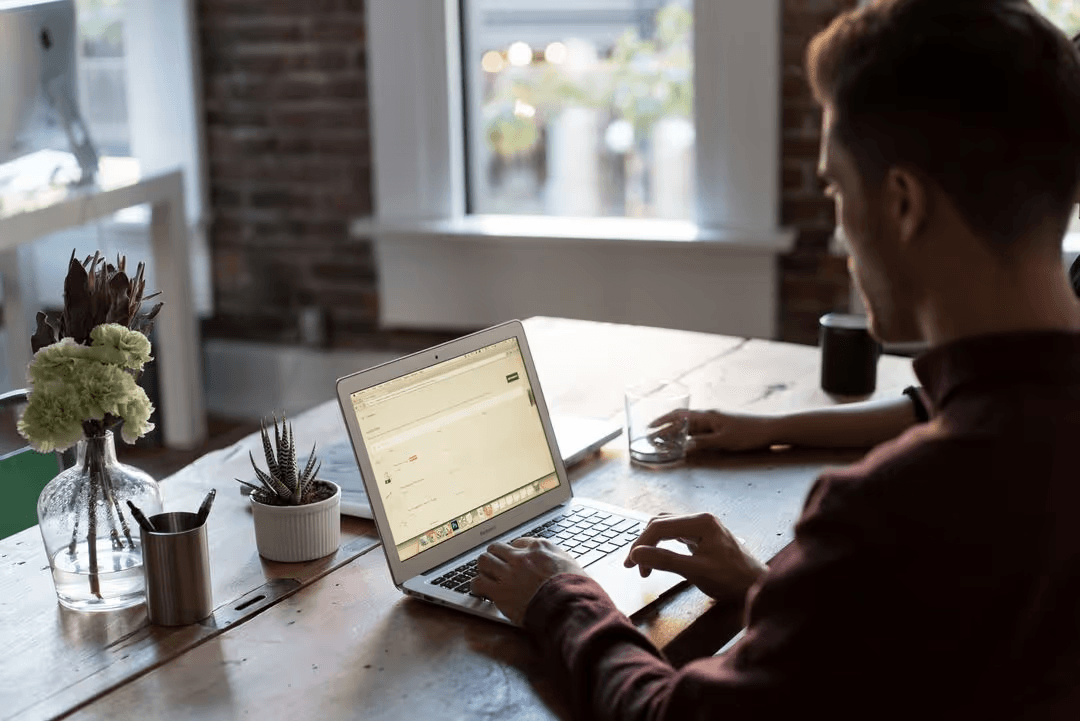 Image of a man working on a macbook taken from behind - Questions to ask yourself before developing a social media strategy - Image