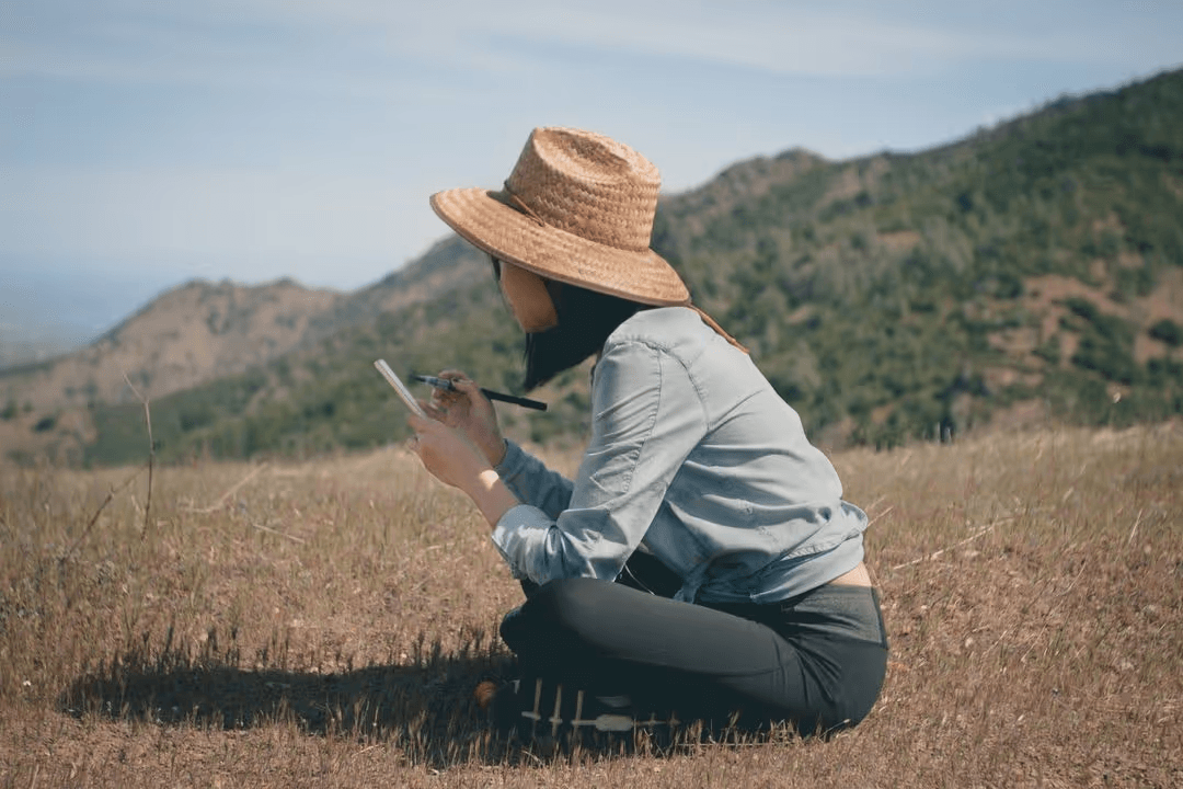 Image of a woman sitting in a field writing on a notepad - How to make a beautiful mood board with free online tools - Image