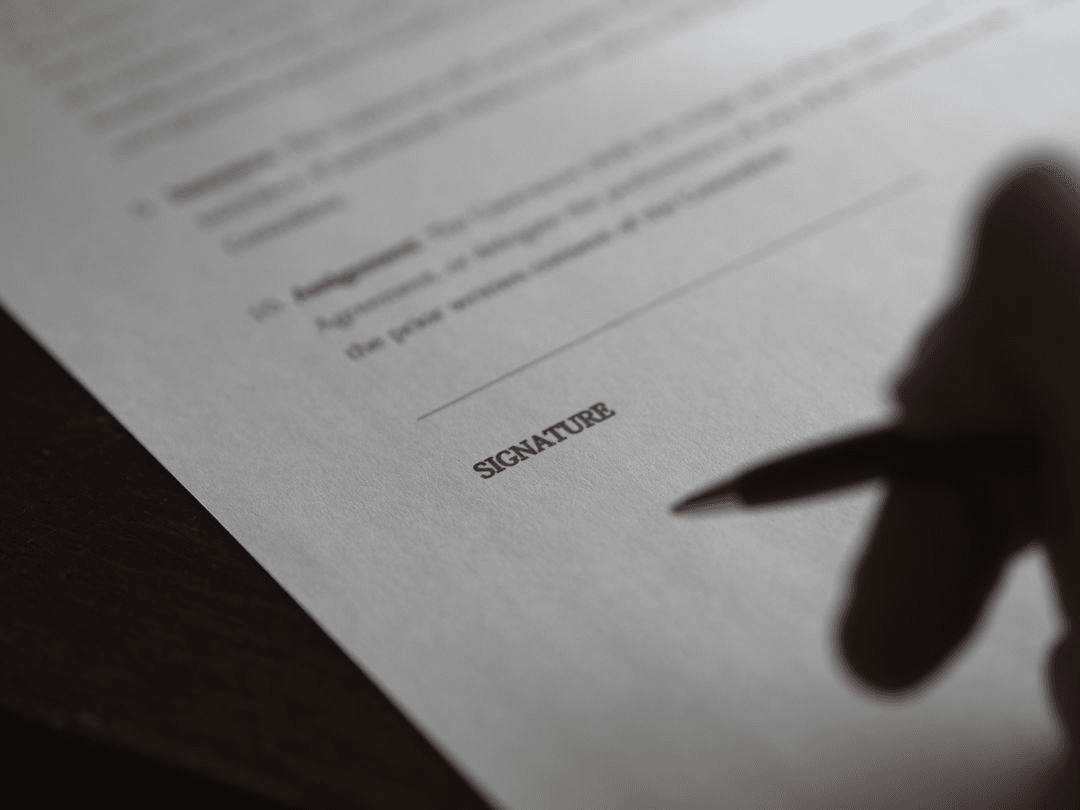Image of a person holding a pen over the signature section of a blurred contract - How to make a beautiful digital vision board with free online tools in 5 steps - Image