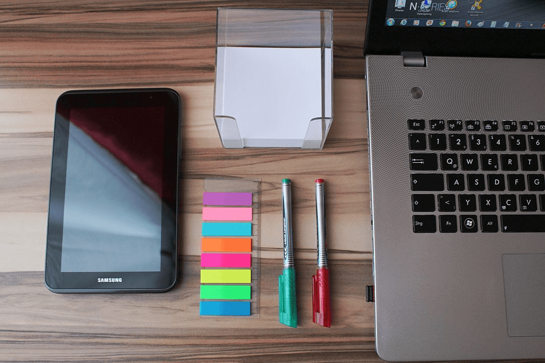 Image of a desk with a laptop, a tablet and sticky notes - Start developing your strategy by conducting a social media audit - Image