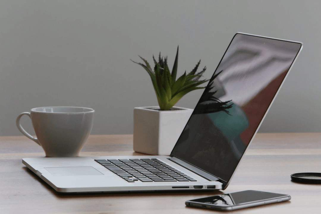 Image of a laptop and a cup on a desk with a plant in the background - Tips on how to choose metrics for your social media strategy - Image