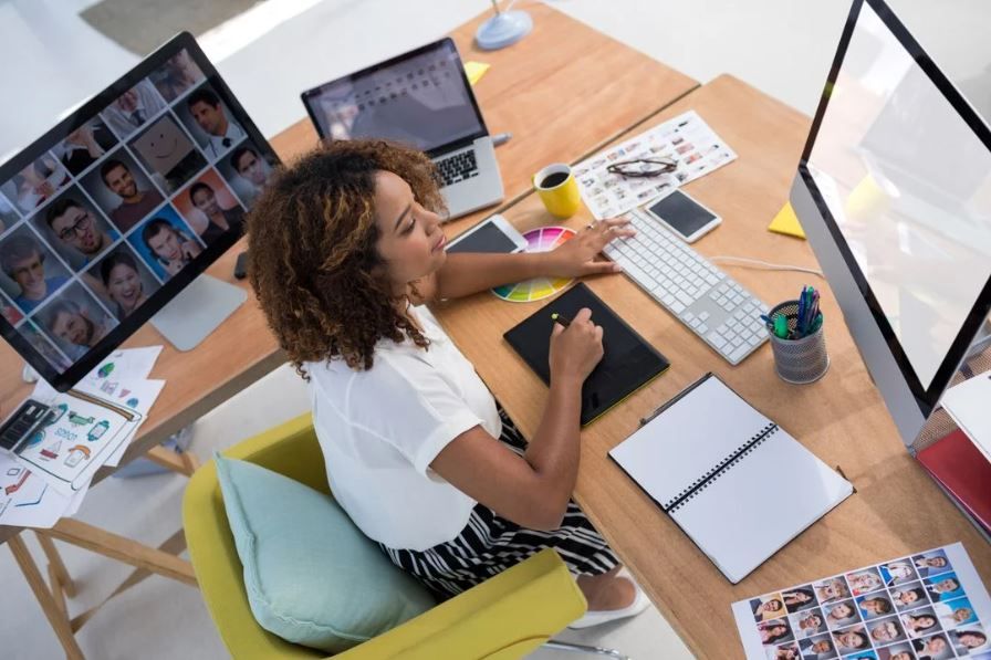 A female graphic designer works with a graphics tablet in front of a monitor - Daily habits of successful designers - Image