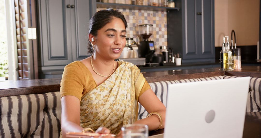 Indian Woman in Sari Multitasking with Laptop in Kitchen
