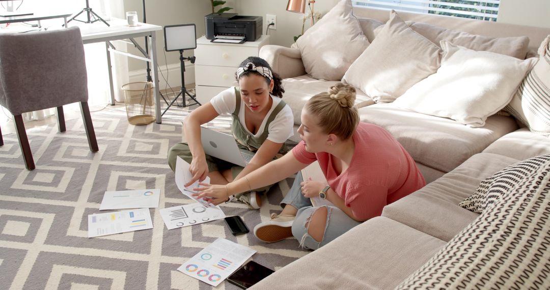 Diverse Female Friends Collaborating on Charts at Home with Digital Devices