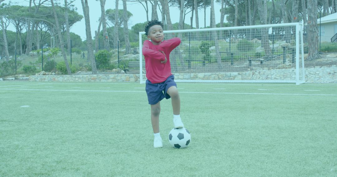 Young boy balancing on soccer ball on outdoor pitch practicing ball control and confidence