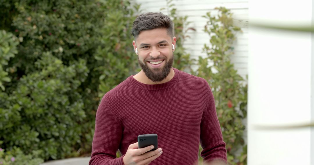 Smiling Man with Smartphone and Earbuds in Sunny Garden
