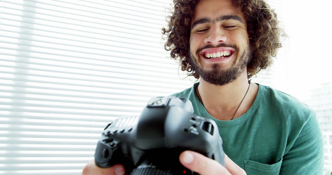 Smiling man reviewing photos on DSLR camera, curly hair, green shirt - Free Images, Stock Photos and Pictures on Pikwizard.com