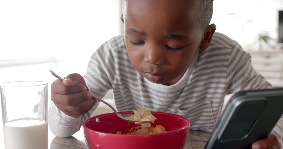 Young boy having breakfast using smartphone display - Free Images, Stock Photos and Pictures on Pikwizard.com